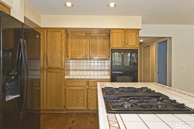 kitchen with black appliances, tile counters, dark hardwood / wood-style floors, and tasteful backsplash