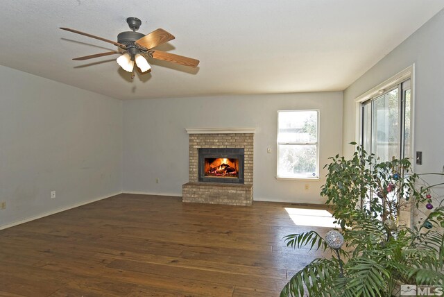 unfurnished living room featuring dark wood-type flooring, ceiling fan, and a brick fireplace