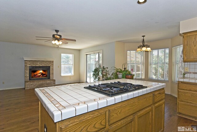 kitchen with hanging light fixtures, stainless steel gas cooktop, dark hardwood / wood-style floors, tile counters, and a center island