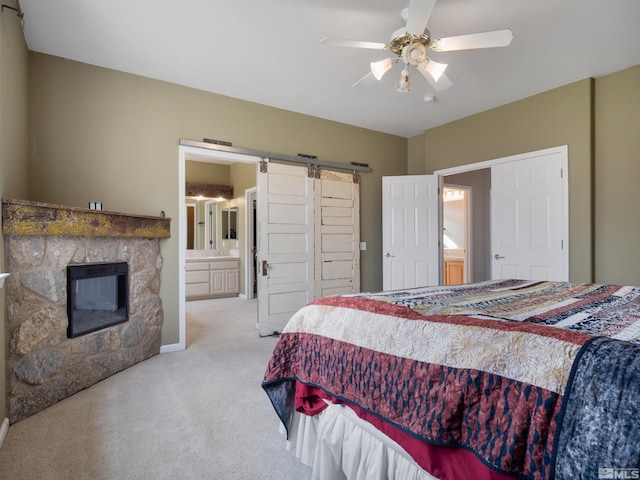 bedroom with ceiling fan, a stone fireplace, a barn door, light carpet, and ensuite bathroom