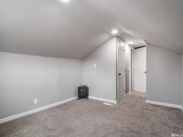 additional living space with vaulted ceiling, a textured ceiling, and carpet flooring