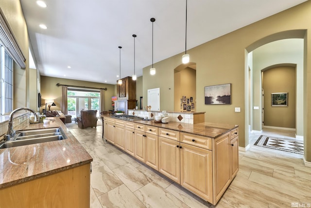 kitchen featuring dark stone counters, sink, stainless steel gas cooktop, hanging light fixtures, and a kitchen island