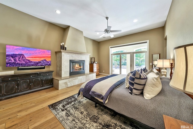 bedroom featuring light hardwood / wood-style flooring, a tiled fireplace, and ceiling fan