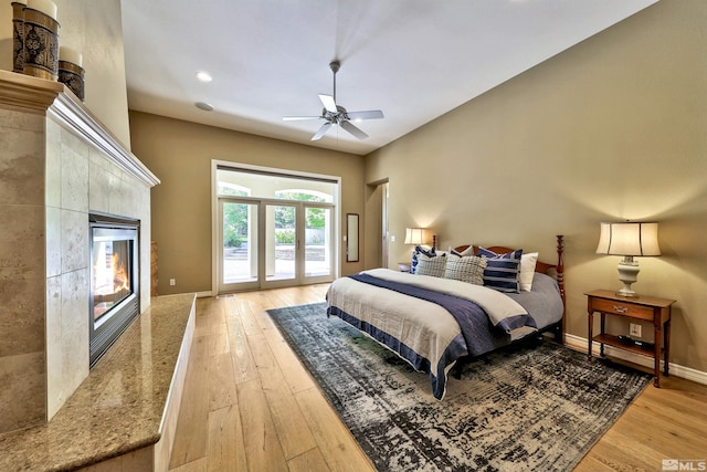 bedroom featuring access to outside, light hardwood / wood-style flooring, a high end fireplace, and ceiling fan