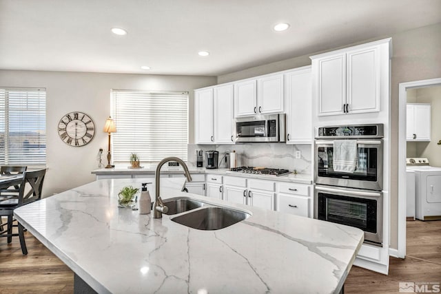 kitchen with light stone countertops, a kitchen island with sink, appliances with stainless steel finishes, and sink