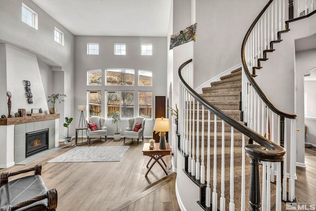 stairway featuring wood-type flooring, a towering ceiling, and a tile fireplace