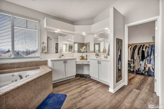 bathroom featuring a relaxing tiled tub, wood-type flooring, and vanity