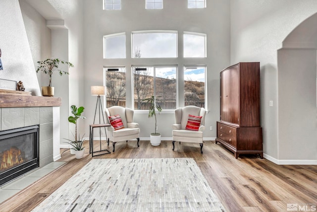 sitting room featuring light wood-type flooring, a fireplace, and a towering ceiling