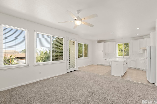 kitchen featuring white cabinets, ceiling fan, light colored carpet, and a kitchen island