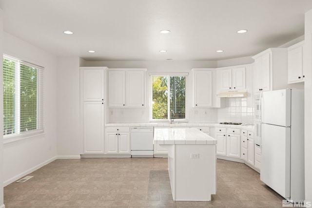 kitchen featuring white appliances, white cabinetry, a kitchen island, and backsplash