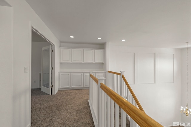 corridor with a notable chandelier and dark colored carpet