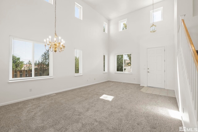 carpeted spare room with plenty of natural light, a high ceiling, and a chandelier