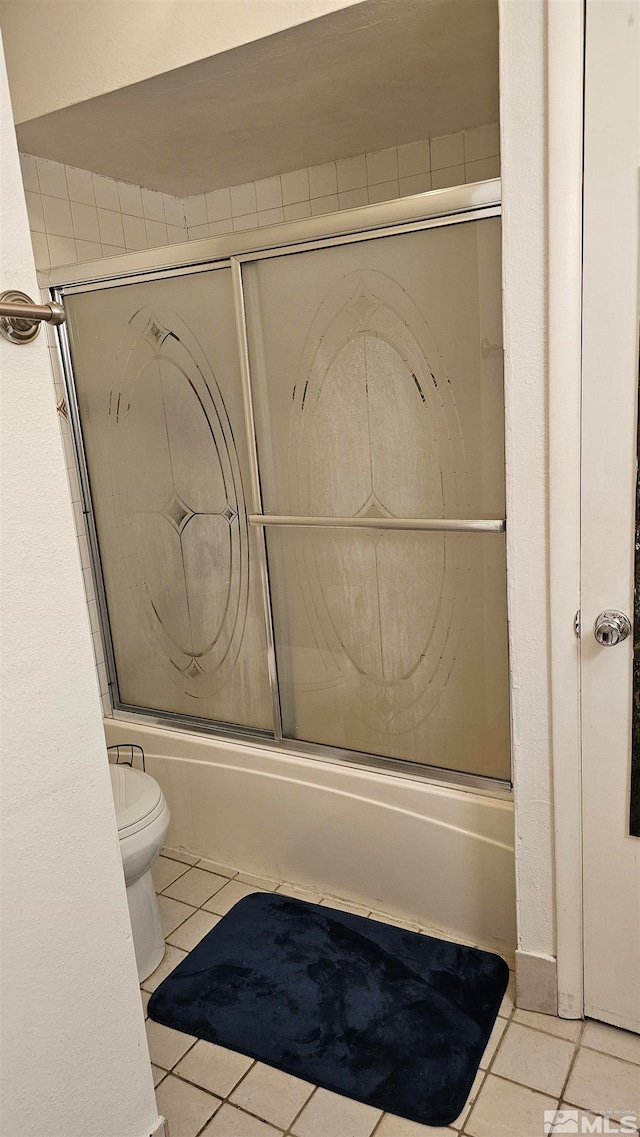 bathroom with tile patterned flooring, bath / shower combo with glass door, and toilet