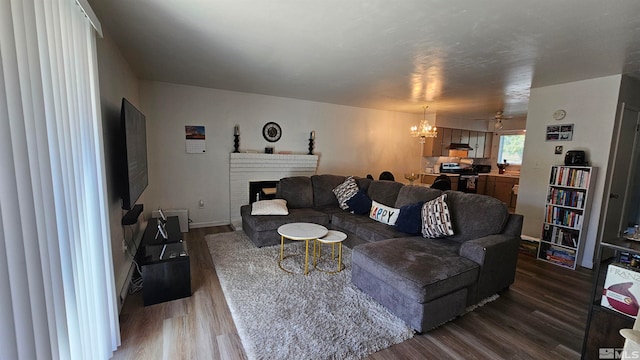 living room featuring a brick fireplace, ceiling fan with notable chandelier, and dark wood-type flooring