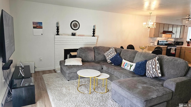 living room with ceiling fan with notable chandelier, a fireplace, and light hardwood / wood-style flooring