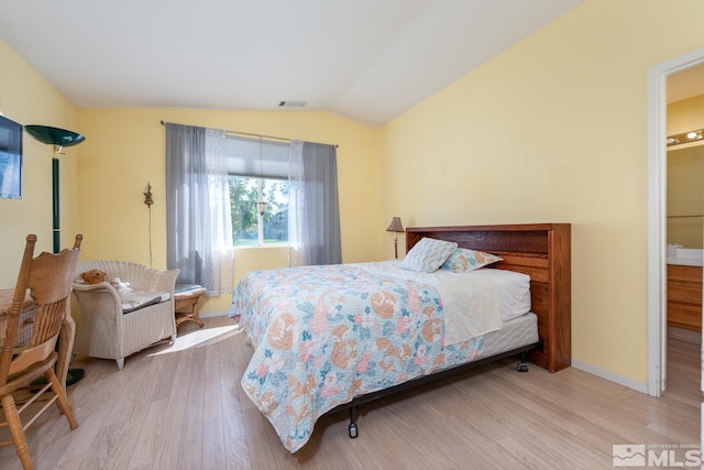 bedroom featuring light wood-type flooring, ensuite bathroom, and lofted ceiling