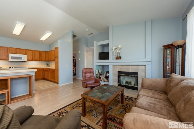 living room with light wood-type flooring, a tiled fireplace, and high vaulted ceiling