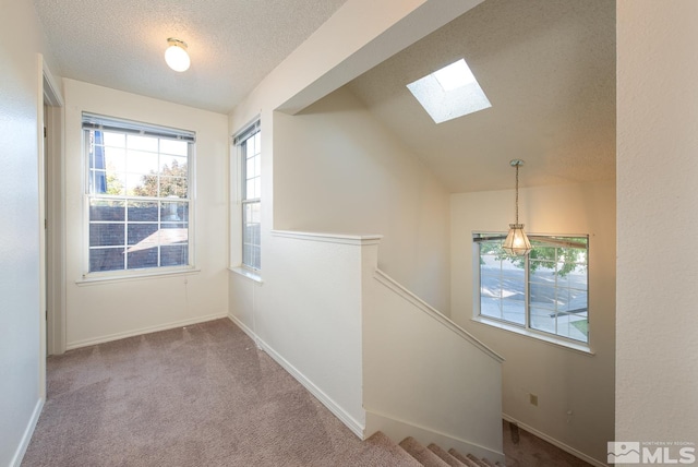 hallway with a textured ceiling, light colored carpet, and lofted ceiling with skylight