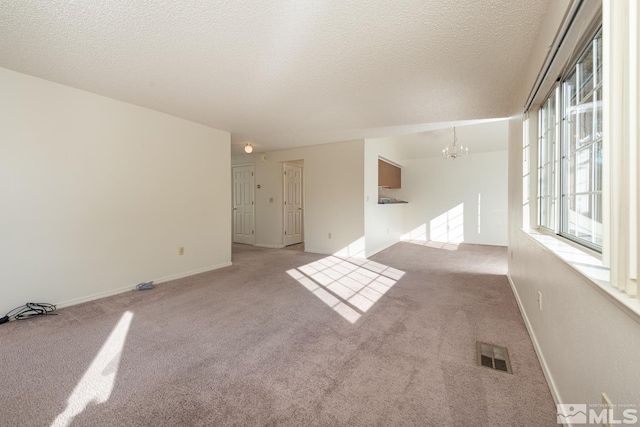 carpeted spare room with a textured ceiling and a notable chandelier