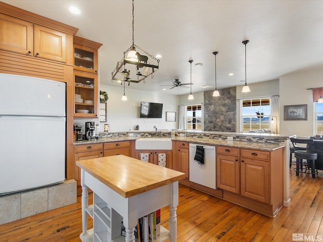 kitchen featuring sink, kitchen peninsula, white appliances, ceiling fan with notable chandelier, and light hardwood / wood-style floors