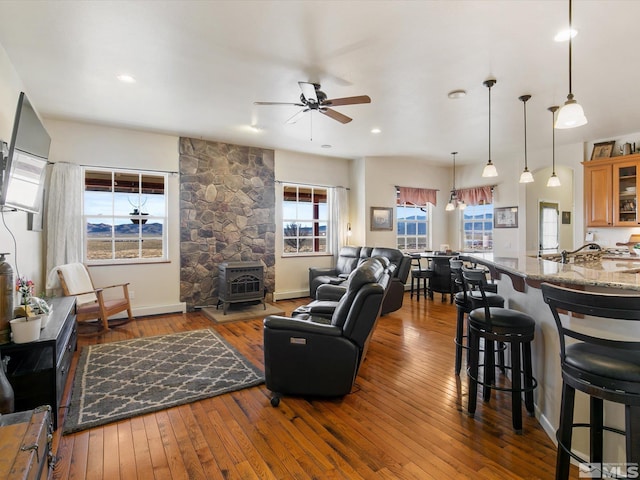 living room featuring a wood stove, ceiling fan, and wood-type flooring