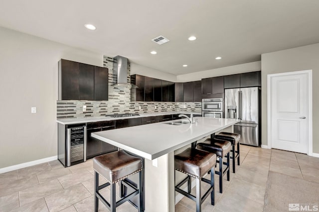 kitchen featuring sink, wall chimney exhaust hood, backsplash, appliances with stainless steel finishes, and a breakfast bar