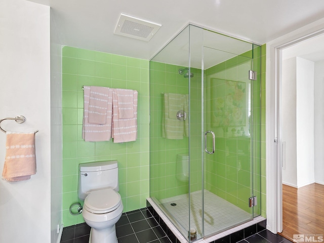 bathroom with hardwood / wood-style flooring, tile walls, a shower with shower door, and toilet