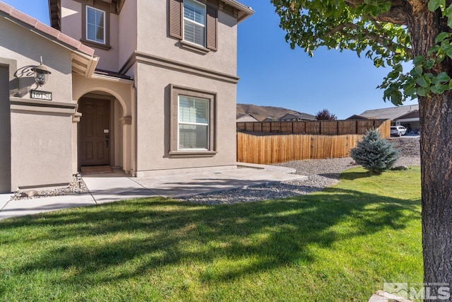 entrance to property with fence, stucco siding, and a lawn