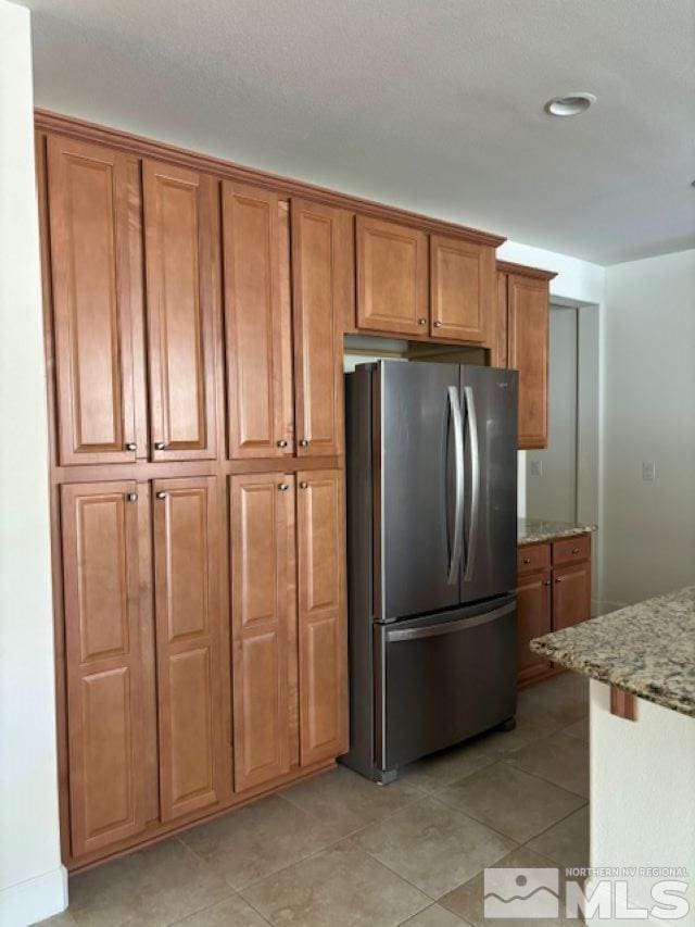 kitchen featuring light stone counters, light tile patterned floors, and stainless steel fridge