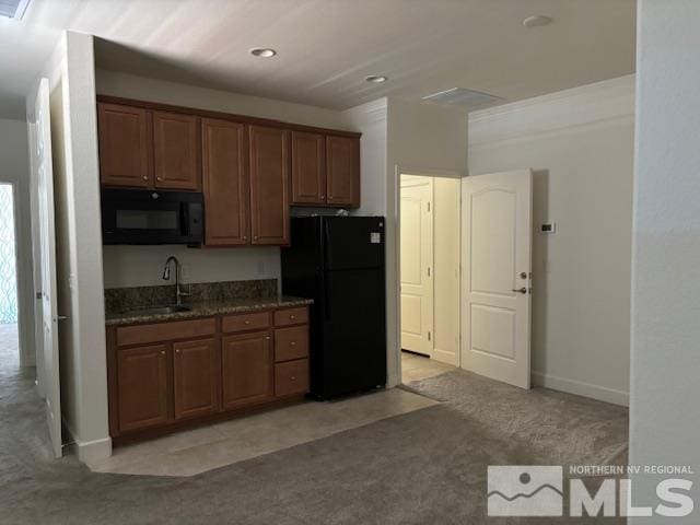 kitchen featuring dark stone countertops, light colored carpet, sink, and black appliances