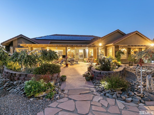 back of house featuring roof mounted solar panels, a tile roof, stucco siding, and a patio area