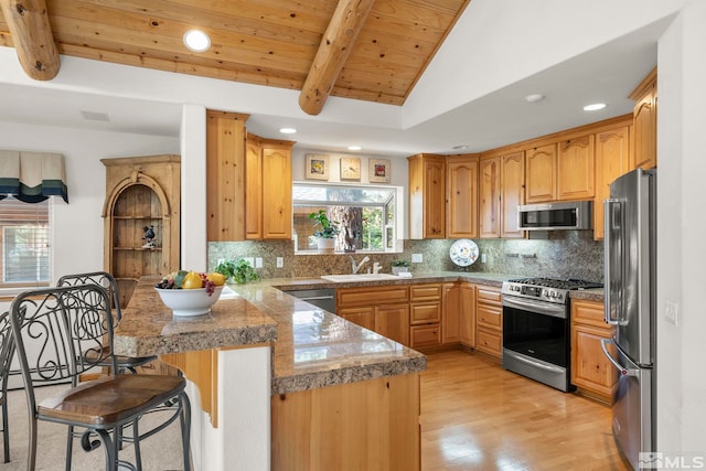 kitchen with kitchen peninsula, stainless steel appliances, lofted ceiling with beams, a breakfast bar, and light wood-type flooring