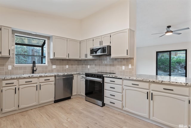 kitchen with sink, light hardwood / wood-style flooring, appliances with stainless steel finishes, light stone countertops, and ceiling fan