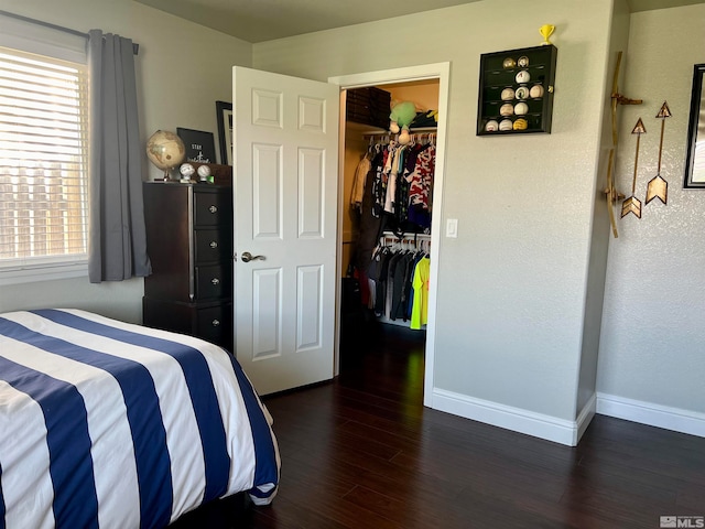 bedroom featuring wood finished floors, a closet, a walk in closet, and baseboards