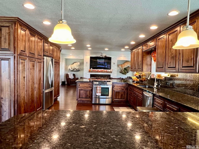 kitchen with a textured ceiling, a peninsula, a sink, appliances with stainless steel finishes, and dark stone counters