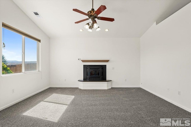 unfurnished living room featuring dark carpet, vaulted ceiling, ceiling fan, and a wood stove