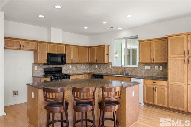 kitchen with a kitchen island, a breakfast bar area, light hardwood / wood-style floors, and black appliances