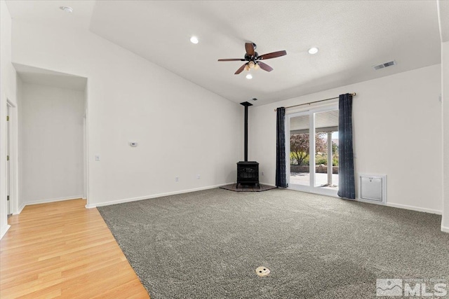 unfurnished living room with ceiling fan, hardwood / wood-style flooring, vaulted ceiling, and a wood stove