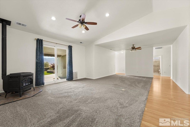 unfurnished living room featuring ceiling fan, hardwood / wood-style floors, vaulted ceiling, and a wood stove