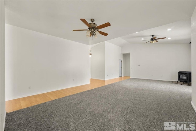 unfurnished living room with a wood stove, vaulted ceiling, ceiling fan, and hardwood / wood-style floors