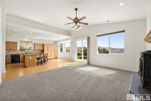 living room with vaulted ceiling, a mountain view, a wood stove, light wood-type flooring, and ceiling fan