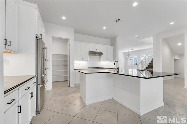 kitchen with white cabinets, an island with sink, high end fridge, and tasteful backsplash