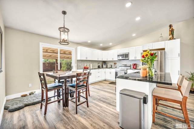 kitchen featuring a breakfast bar, white cabinets, vaulted ceiling, light hardwood / wood-style flooring, and stainless steel appliances