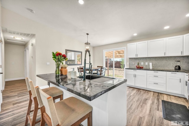 kitchen featuring a kitchen breakfast bar, light hardwood / wood-style floors, white cabinetry, and pendant lighting