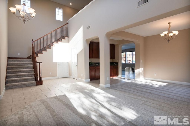 unfurnished living room featuring a high ceiling, a chandelier, and light colored carpet