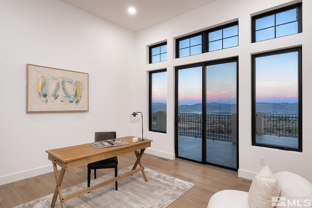 home office with a high ceiling, light hardwood / wood-style flooring, and a mountain view