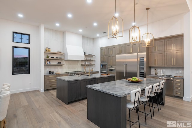 kitchen with custom exhaust hood, sink, decorative light fixtures, a center island with sink, and appliances with stainless steel finishes