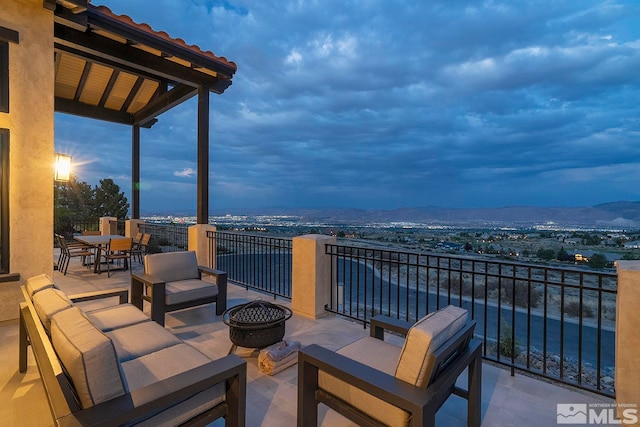 patio terrace at dusk featuring a balcony, an outdoor living space with a fire pit, and a mountain view