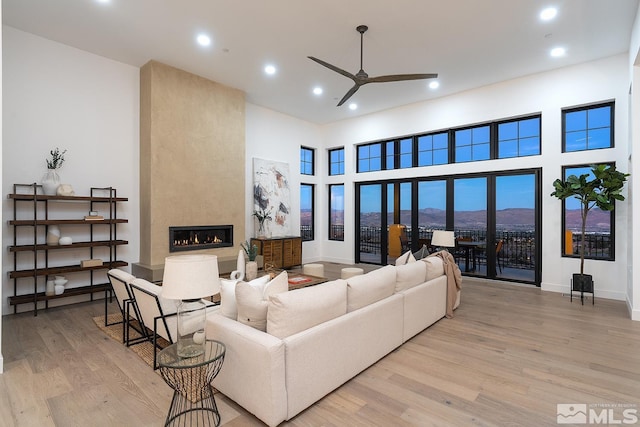 living room with light hardwood / wood-style floors, a fireplace, ceiling fan, and a high ceiling