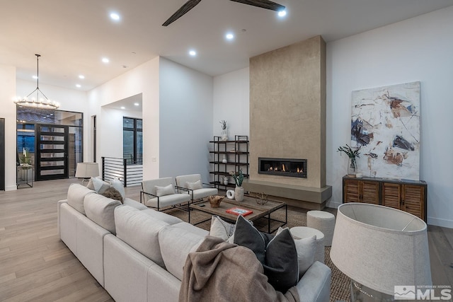 living room featuring ceiling fan with notable chandelier, a large fireplace, and light hardwood / wood-style flooring